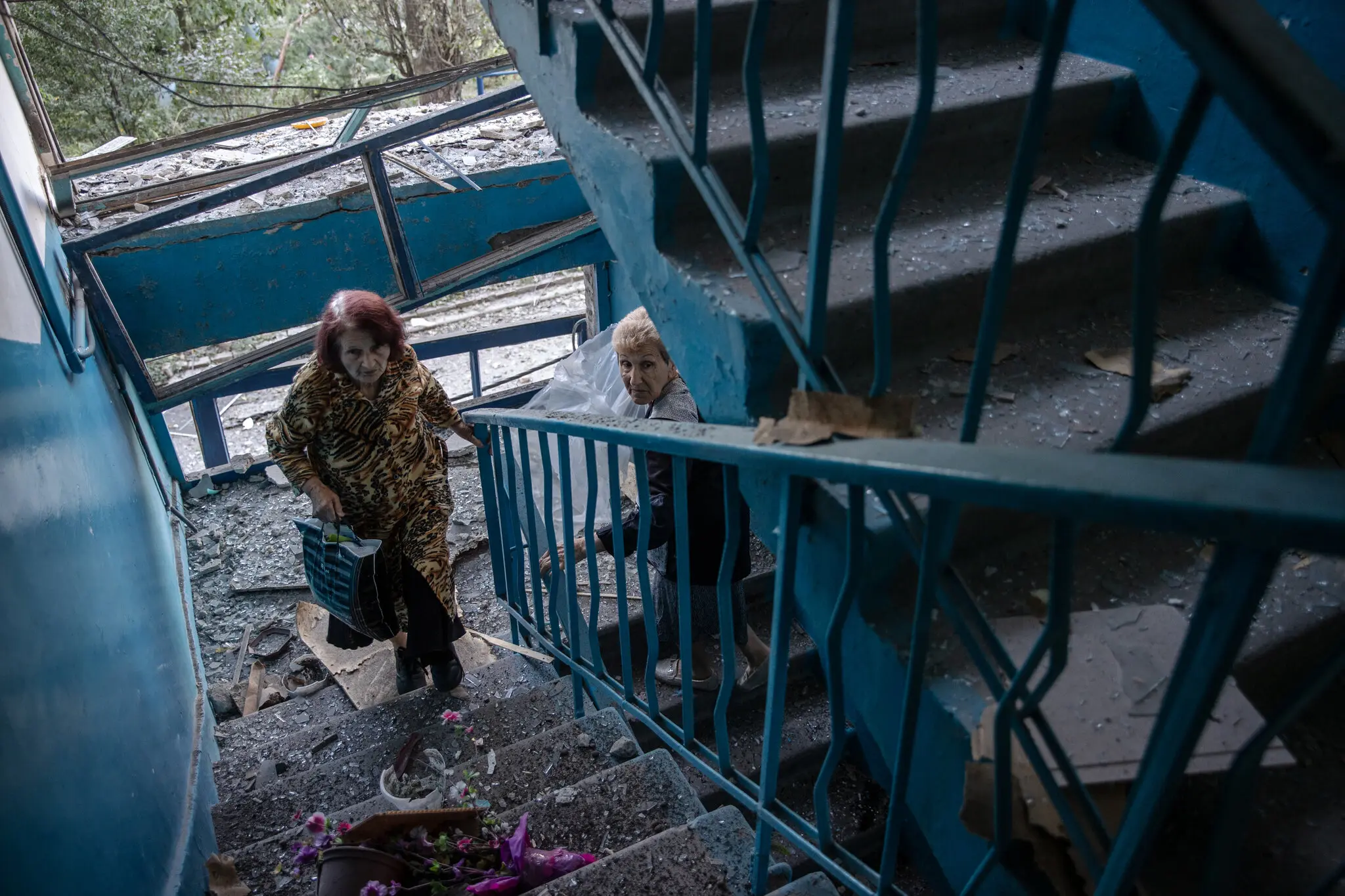 Жінки обережно ходять по склу та пилу на сходах у пошкодженій будівлі наступного дня після російської атаки в Покровську, Україна, 8 серпня